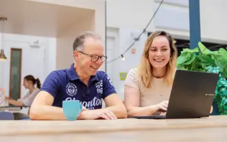 Oudere man en studente aan tafel op laptop atrium